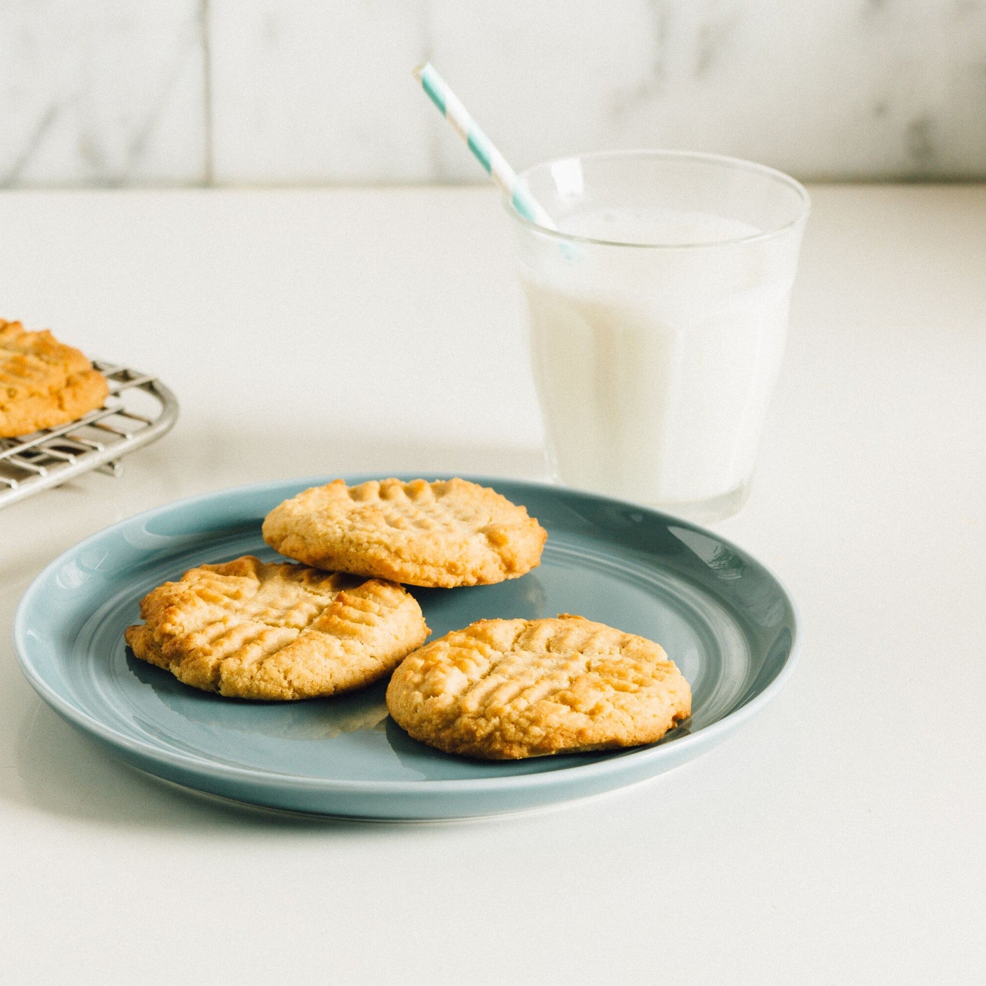 PB2 Organic Peanut Butter Cookies on a plate with a glass of milk with a straw behind them. 