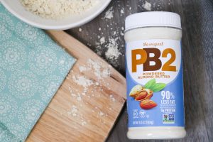PB2 Powdered Almond butter jar sitting on table top next to a cutting board and napkin.
