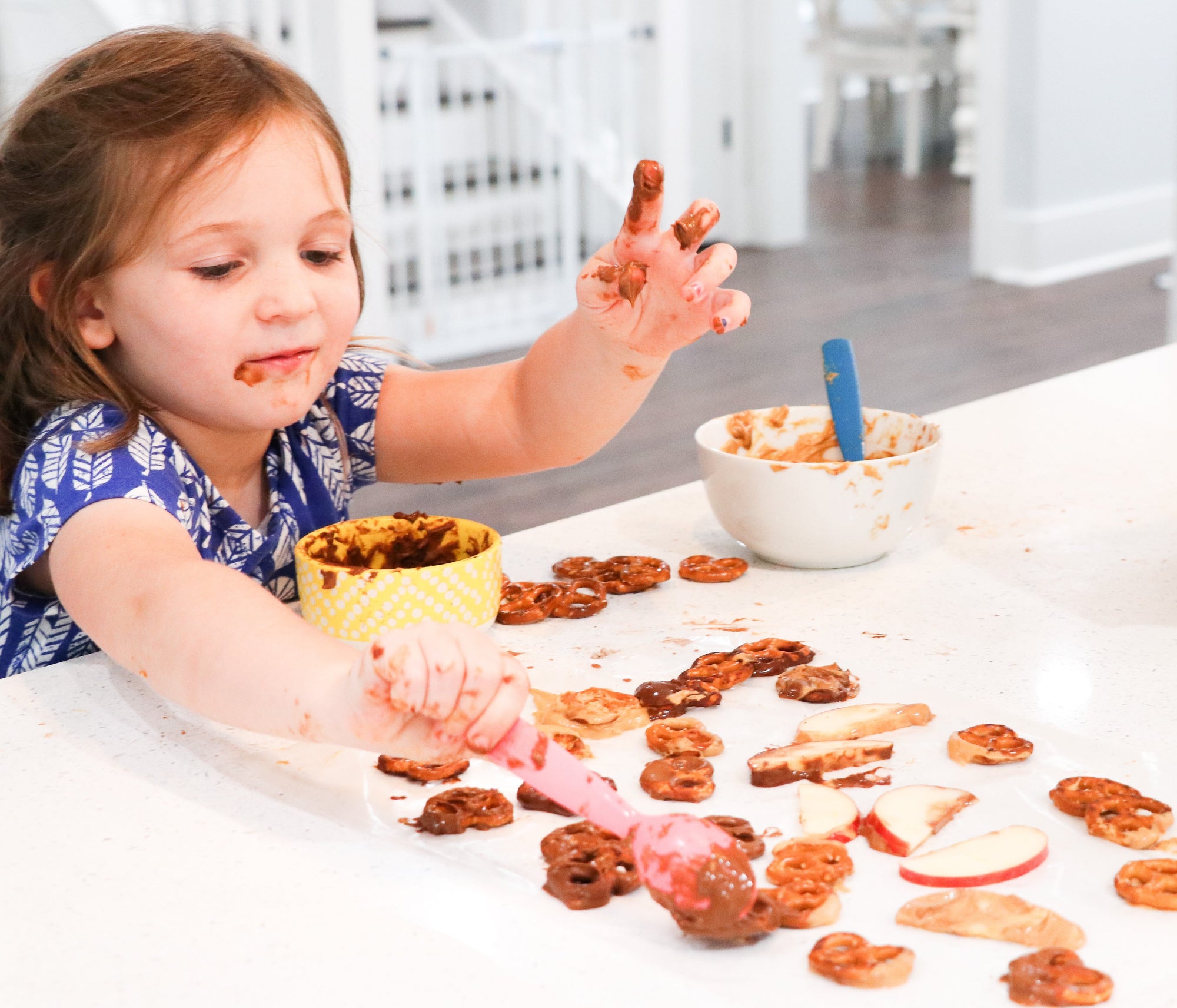 Little girl making snacks using PB2 Original and PB2 with Cocoa. Dipping pretzels and apples into the PB2. 