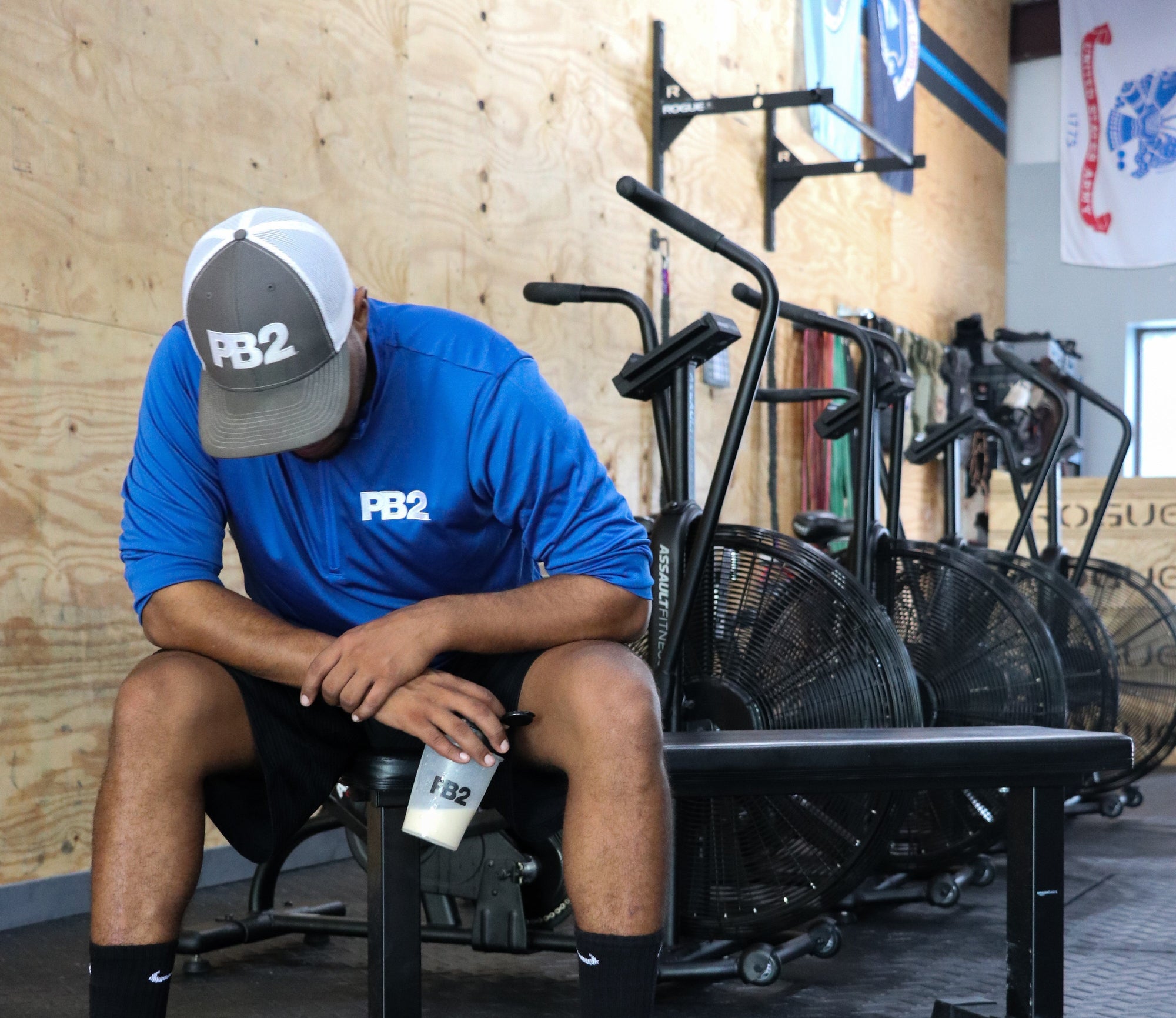 PB2 team member in gym sitting on bench with a PB2 shaker cup.