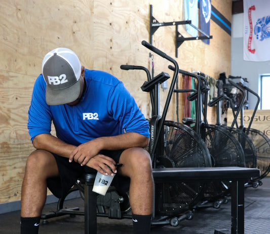 PB2 team member in gym sitting on bench with a PB2 shaker cup.